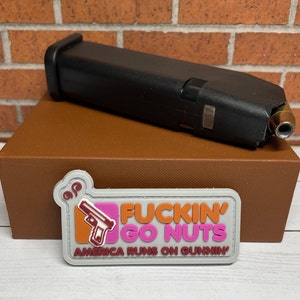 May include: A gray patch with the text "Fuckin' Go Nuts" in pink and orange letters. Below the text is "America Runs On Gunnin'" in smaller pink letters. A cartoon gun is in the upper left corner of the patch.