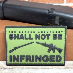 May include: A green patch with the text "THE SECOND AMENDMENT SHALL NOT BE INFRINGED" and illustrations of two rifles. A black magazine is in the background.
