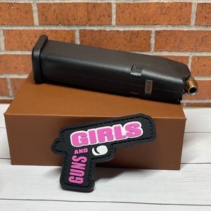 May include: A black and pink patch with the text "Girls and Guns" in a gun shape.