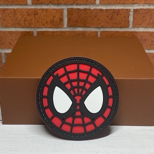 May include: A red and black round patch with a white spider-man face and web design.