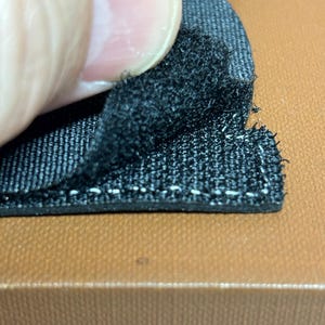 Peut inclure: Gros plan sur un tissu noir avec une texture duveteuse. Le tissu est fix&eacute; &agrave; une surface brune avec des coutures blanches.