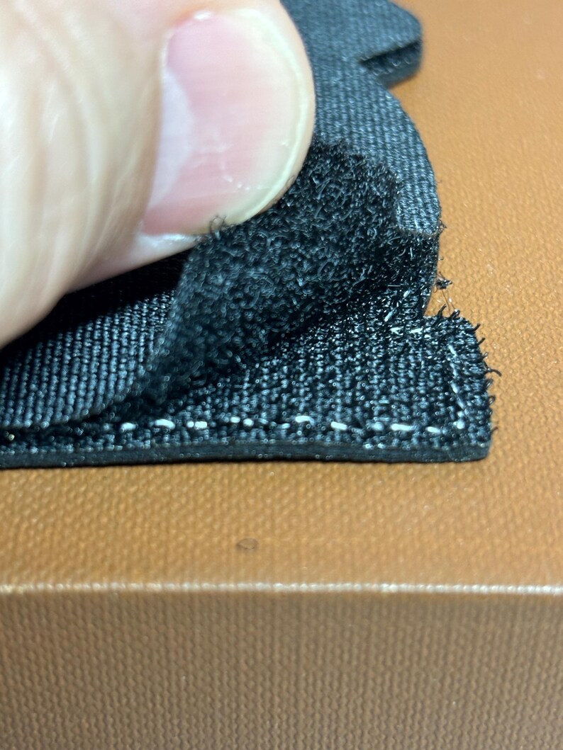 Peut inclure: Gros plan sur un tissu noir avec une texture duveteuse. Le tissu est fix&eacute; &agrave; une surface brune avec des coutures blanches.
