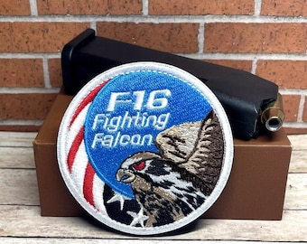 May include: A white, red, and blue embroidered patch with the text "F16 Fighting Falcon" and a falcon illustration.