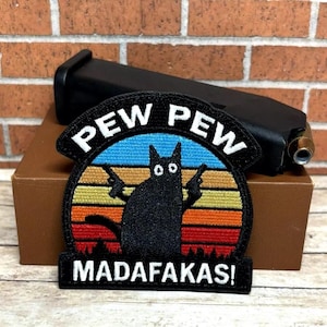 May include: Black cat holding two guns with a sunset behind it. The text "PEW PEW MADAFAKAS!" is on the patch.