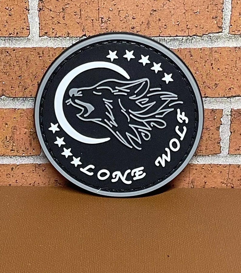 May include: Black and white embroidered patch with a wolf howling at the moon. The patch has five stars around the moon and the words "Lone Wolf" written below the moon.