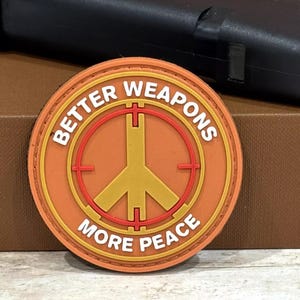 May include: A round orange patch with a white outline and the text "Better Weapons More Peace" in white. A red target symbol with a yellow peace sign inside is in the center.
