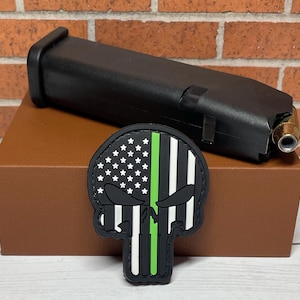 May include: Black and white skull patch with a green thin line down the center. The skull is wearing a US flag bandana. The patch is on a brown surface.