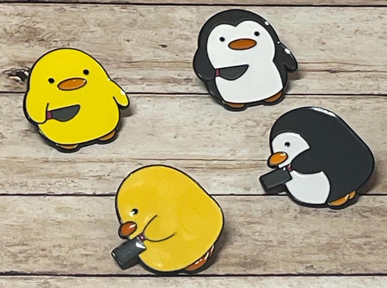 May include: Four enamel pins featuring cartoon animals holding knives. Two yellow chicks and two black and white penguins.