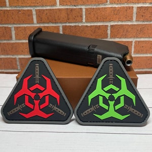 May include: Two triangular patches with a biohazard symbol and three knives inside. One patch is red and the other is green.