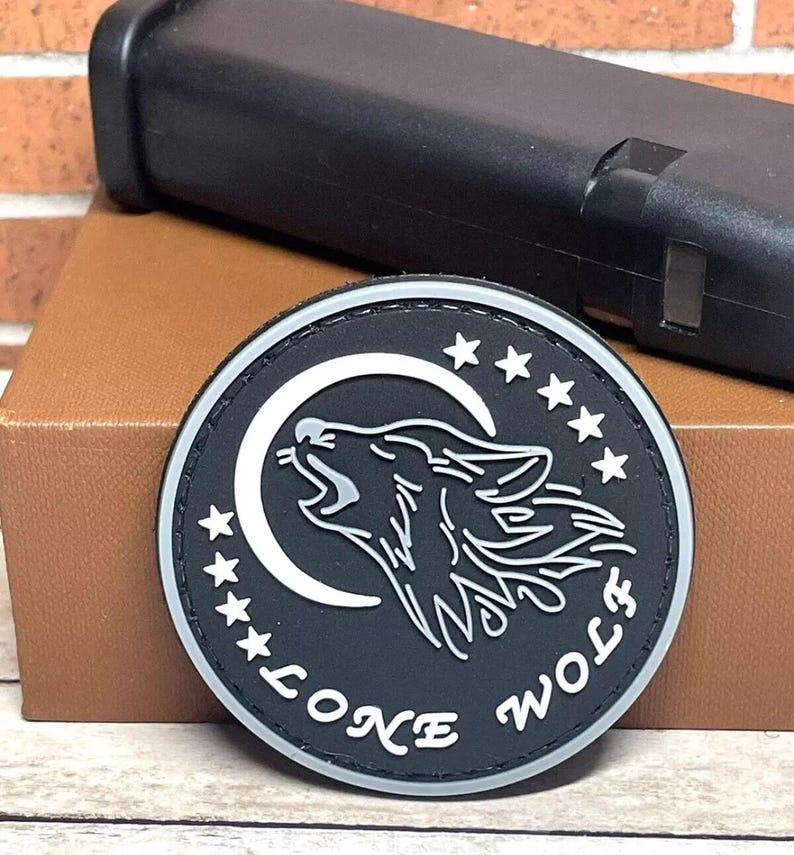 May include: Black and white embroidered patch with a wolf howling at the moon. The patch has five stars and the text "Lone Wolf" around the edge.
