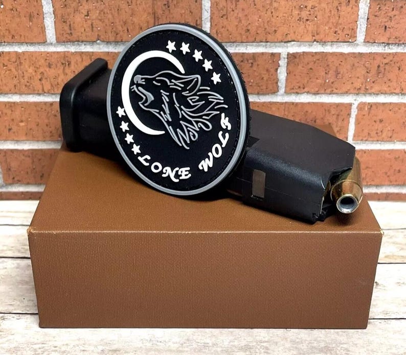 May include: A black and white patch with a wolf howling at the moon. The patch has a white border with stars and the text "Lone Wolf" around the edge.
