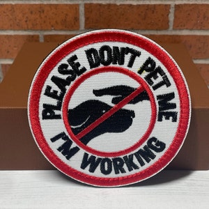May include: Red and white embroidered patch with the text "Please Don't Pet Me I'm Working" and a black silhouette of a hand with a red line through it.