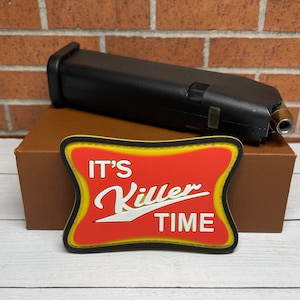 May include: A red and yellow patch with the text "It's Killer Time" on a brown box. The patch is a morale patch with a humorous and edgy design.