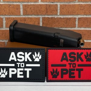 May include: Two black and red patches with white text that reads "Ask to Pet" with a paw print graphic. The patches are on a brick background.
