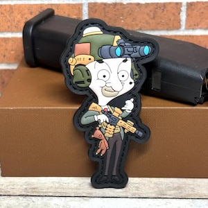 May include: A black and white cartoon character wearing a green military helmet with a night vision scope, holding a rifle and a teddy bear. The character is wearing a black suit and a red tie. The patch is made of black fabric with a white outline.
