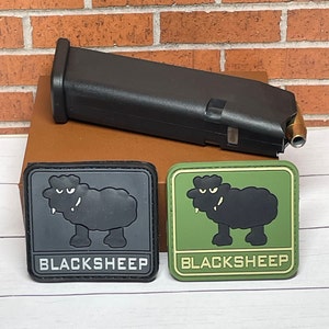 May include: Two black and white sheep patches with the text "BLACKSHEEP" on a green and gray background. The patches are on a brown surface.