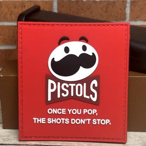 May include: Red square patch featuring the Pringles mascot with a black mustache and the word "PISTOLS" in a white and brown font. The text "ONCE YOU POP, THE SHOTS DON'T STOP" is below the word "PISTOLS".