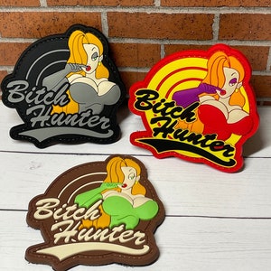May include: Three embroidered patches featuring a cartoon character with red, green, and gray clothing. Each patch has the text "Bitch Hunter" in a stylized font.