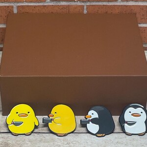 May include: Four enamel pins featuring cartoon animals holding bowls. Two yellow chicks and two black and white penguins.