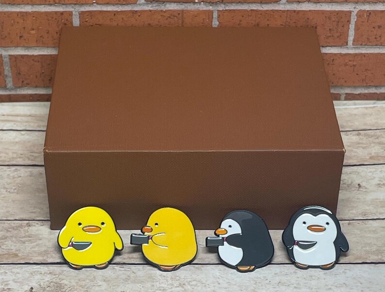 May include: Four enamel pins featuring cartoon animals holding bowls. Two yellow chicks and two black and white penguins.
