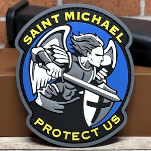May include: A circular patch featuring Saint Michael, with the text "SAINT MICHAEL PROTECT US". The design includes an angel with a sword and shield, set against a blue and black background, with yellow lettering.