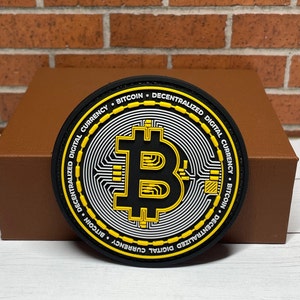 May include: Black and yellow circular patch with the Bitcoin logo and the text "Decentralized Digital Currency - Bitcoin" repeated around the edge.