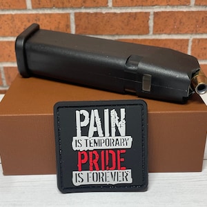 May include: Black patch with white text that reads "Pain is temporary, Pride is forever". The patch is on a brown box with a black magazine on top.