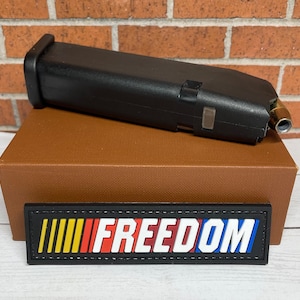 May include: A black magazine with a gold bullet tip, sitting on a brown box with a black patch that says "FREEDOM" in white letters with red, yellow, and blue stripes.