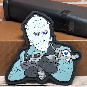May include: A patch featuring a cartoon figure in a hockey mask, holding a rifle. The figure is wearing a blue uniform with a patch on the arm. The patch has a black border.