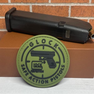 May include: Green and black patch with the words "Glock Safe Action Pistols" and a silhouette of a handgun with the words "Lock Perfection" inside a circle.