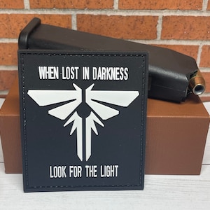 May include: Black and white patch with a firefly design and the text "WHEN LOST IN DARKNESS LOOK FOR THE LIGHT".