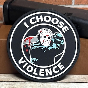 May include: Black and white round patch with a white border. The patch features a cartoon image of a hockey mask-wearing figure holding a bloody knife. The text "I CHOOSE VIOLENCE" is written in white around the image.