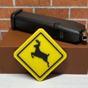 May include: Yellow and black warning sign with a deer silhouette. The sign is a patch with a diamond shape and a black border. The sign is on top of a brown box.