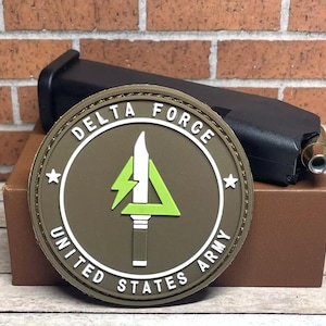 May include: A brown and green embroidered patch with the text "DELTA FORCE UNITED STATES ARMY" and a green lightning bolt inside a triangle.
