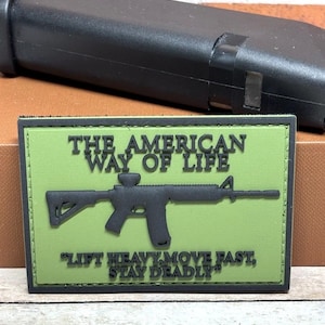 May include: A rectangular patch with a green background and black border. The text "THE AMERICAN WAY OF LIFE" is at the top, with a black rifle graphic below. The text "LIFT HEAVY, MOVE FAST, STAY DEADLY" is at the bottom.