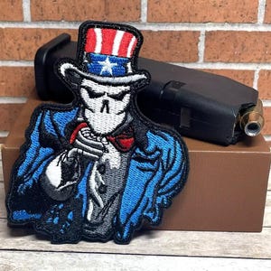 May include: A blue and white embroidered patch of Uncle Sam with a skull face wearing a red, white, and blue top hat. The patch is on a brown surface.