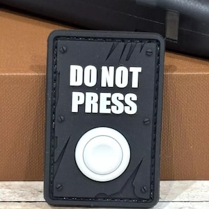 May include: Black and white patch with a white button and the text "DO NOT PRESS" in white letters.