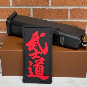 May include: Black patch with red Japanese characters that read "武道" (Budō) on a brown surface.