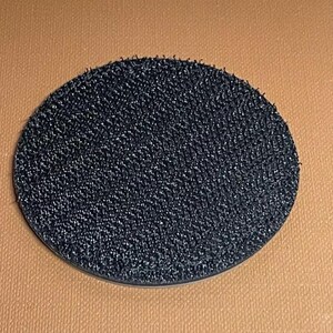 May include: A round, black, adhesive-backed hook and loop fastener. The fastener is made of a soft, fuzzy material.