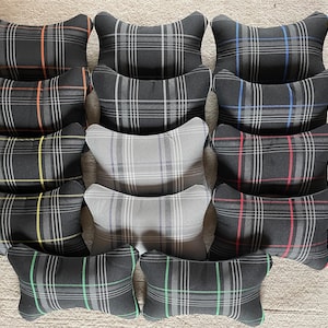May include: A selection of black and grey tartan-patterned cushions with coloured stripes in red, orange, yellow, green, and blue. The cushions are in a distinctive shape and arranged in a grid.