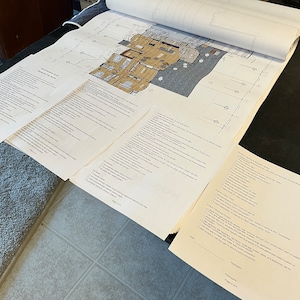 May include: A blueprint of a building with several pages of checklists and forms. The blueprint shows a floor plan with rooms and hallways. The checklists and forms are titled "Pre-Construction Meeting Checklist" and "Punch List".