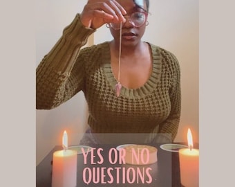 May include: A person wearing glasses and an olive green jumper holds a pendulum over a table with two lit candles. The text "YES OR NO QUESTIONS" is displayed on the table. The pendulum has a pink crystal at the end.