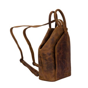 May include: A brown leather backpack with a unique design. The bag has a top handle and adjustable straps. The leather has a distressed look.