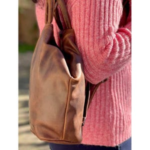 May include: A brown leather backpack with a top handle and adjustable straps. The backpack has a distressed look and is made of high-quality leather.