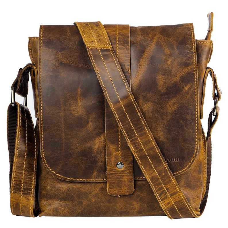 May include: A brown leather messenger bag with a long adjustable strap. The bag has a flap closure with a metal button and a small pocket on the front. The bag has a zippered pocket on the side and the word "WOOD" is visible on the front.