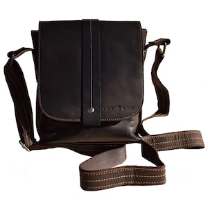 May include: A brown leather messenger bag with a flap closure and an adjustable shoulder strap. The bag has a small pocket on the front with the text "GREEN WOOD" embossed on it.