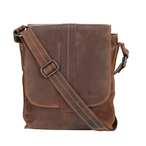 May include: A brown leather messenger bag with a long adjustable strap and a buckle closure. The bag has a flap with a stitched design and a small pocket on the front. The bag has a brand label that says "Leather & Wood".