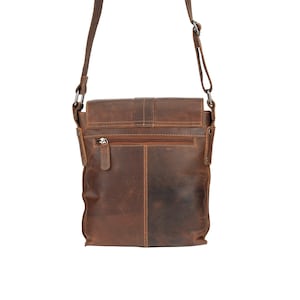 May include: A brown leather crossbody bag with a flap closure and a zippered pocket on the back. The bag has a distressed look and a brown leather strap.