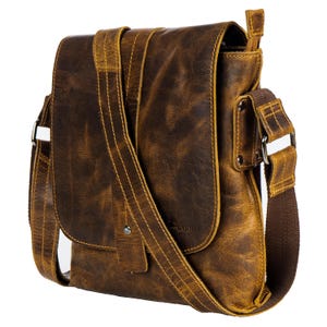 May include: A brown leather messenger bag with a flap closure and an adjustable shoulder strap. The bag has a distressed look and a small pocket on the front. The bag has the word "Wood" embossed on the front.
