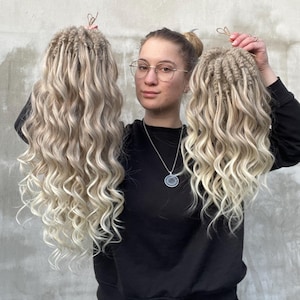 May include: Two sets of long, blonde, curly synthetic dreadlocks. The dreadlocks are held up by a person wearing a black sweatshirt and glasses.